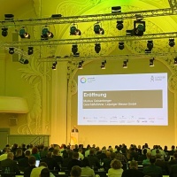 Ein Redner eröffnet vor großem Publikum die protekt 2024 im festlich beleuchteten Saal Ein Redner eröffnet vor großem Publikum die protekt 2024 im festlich beleuchteten Saal