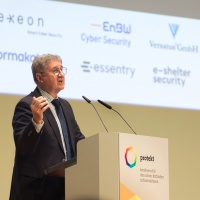 Ein Mann spricht auf der protekt 2024 am Rednerpult mit zwei Mikrofonen, hinter ihm sind die Logos mehrerer Partnerunternehmen auf einer Leinwand zu sehen. Ein Mann spricht auf der protekt 2024 am Rednerpult mit zwei Mikrofonen, hinter ihm sind die Logos mehrerer Partnerunternehmen auf einer Leinwand zu sehen.